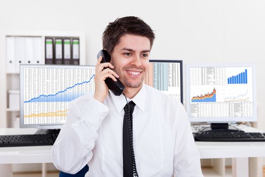 Enthusiastic young male stock broker in a bull market holding a telephone