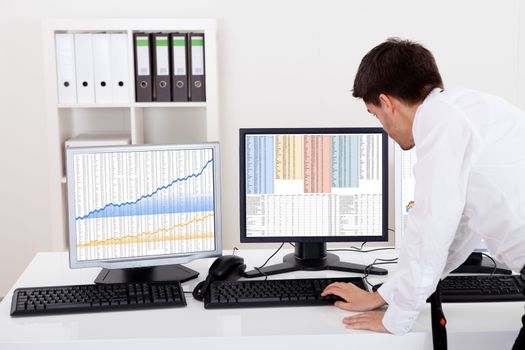 Over the shoulder view of the computer screens of a stock broker trading in a bull market showing ascending graphs