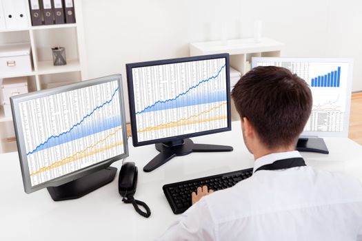 Over the shoulder view of the computer screens of a stock broker trading in a bull market showing ascending graphs