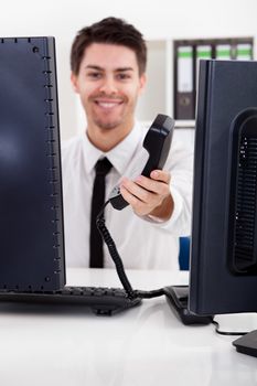 View between two computer monitors of a handsome smiling stock broker with a landline telephone handset in his hand