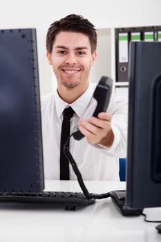 View between two computer monitors of a handsome smiling stock broker with a landline telephone handset in his hand