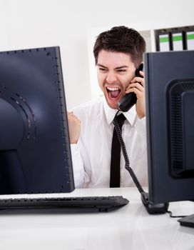 View between two computer monitors of a handsome smiling stock broker with a landline telephone handset in his hand