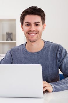 Smiling handsome casual young man sitting at a table using a laptop in a home office