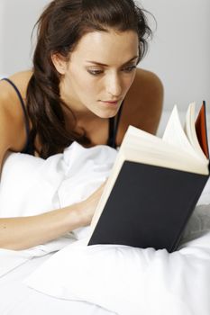 Young woman reading her book in bed