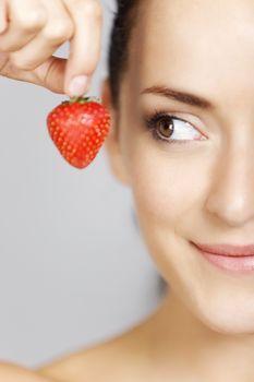 Young woman holding a strawberry in a beauty style pose.