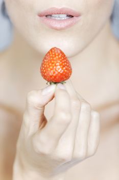 Young woman holding a strawberry in a beauty style pose.