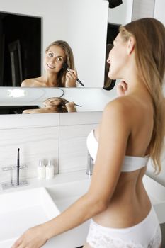 Attractive young woman in underwear applying make up in bathroom.