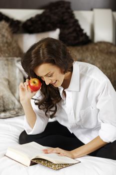 Attractive young woman enjoying a good book in bed.