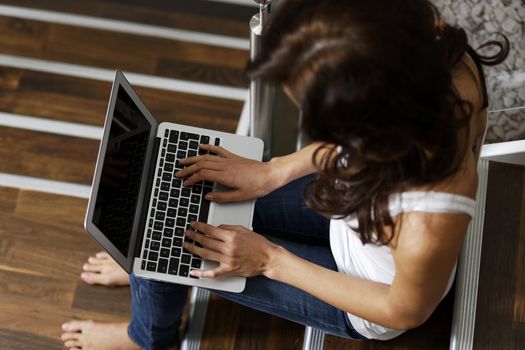 Woman using laptop while sitting on a staircase.