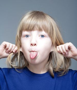 boy with long blond hair sticking out his tongue and pulling ears