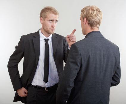 two young businessmen standing, discussing, arguing - isolated on light gray