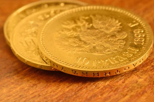 3 gold coins placed on hard old wood. Russian ten rubles value coin on top. Still life with small depth of field. Focus on the edge of first coin.