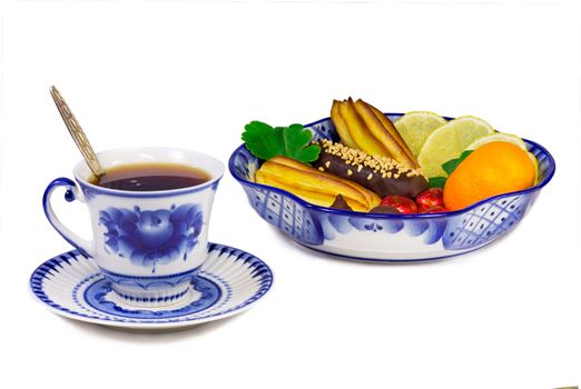 A Cup of tea and a bowl filled with cakes, sweets, fruits. Painted blue pattern in the style of the "Gzhel" and presented on a white background.
