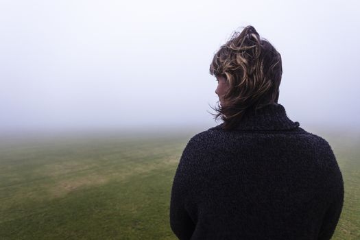 Woman looks into the season mist over the field pending future days.