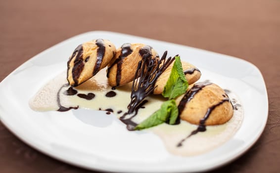 tasty dessert with chocolate, sweet sauce, cakes and mint on a white plate