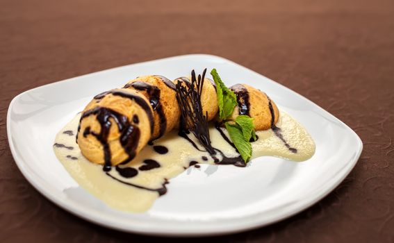 tasty dessert with chocolate, sweet sauce, cakes and mint on a white plate
