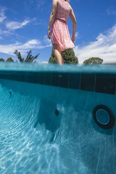 Girl testing pool water by dipping her tocsin to feel the temperature.