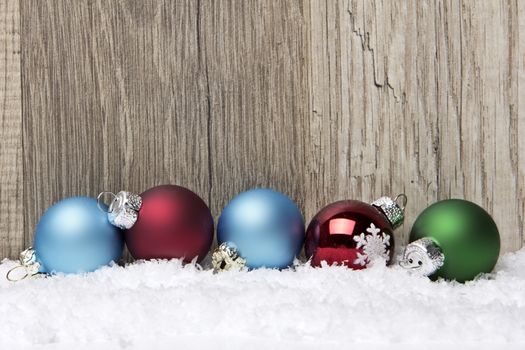 christmas decoration with wooden background, snow, christmas baubles green, blue and red 