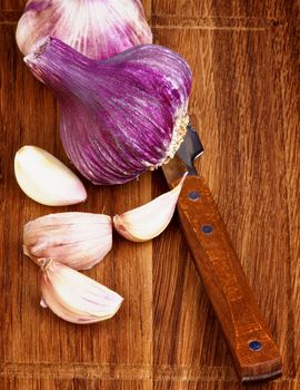 Arrangement of Fresh Pink Garlic Full Body and Slices with Kitchen Knife on Wooden Cutting Board closeup