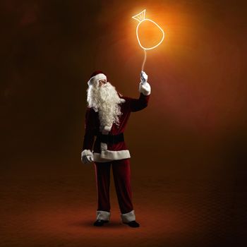 Santa Claus is holding a shining symbol of the bag with gifts on a string