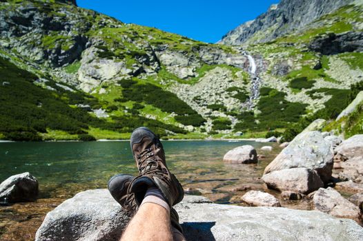Hiker resting over the glacier lake with a waterfall in the background in high mountains
