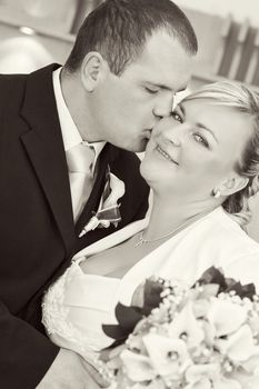 beautiful young wedding couple, bride with bouquet kissed by her groom, black and white tone