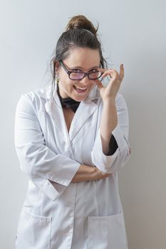 thirtie something brunette woman wearing a lab coat holding her glasses with a big funny smile