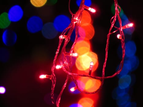 A red light bulbs wire string on the backdrop of other colors blurred light for festive Christmas or Diwali decoration.