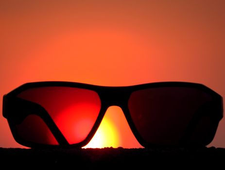 A metaphorical picture of sunglasses against the backdrop of the setting sun conceptualizing a holiday.                               