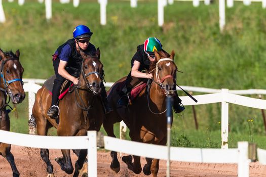 Jockeys riding together close focusing on race horses galloping on sand track training