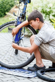Teenager repairing his bike, using spanner to change broken tyre, outdoor shoot