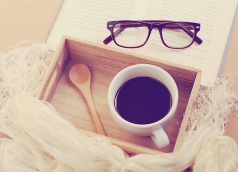 Eyeglasses and book with black coffee on wooden tray, retro filter effect