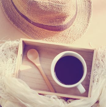 Straw hat with black coffee and spoon on wooden tray, retro filter effect