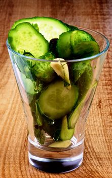 Appetizer with Slices of Delicious Pickled Cucumbers in Brine of Garlic, Dill, Parsley and Black Peppercorn in Glass isolated on Wooden background