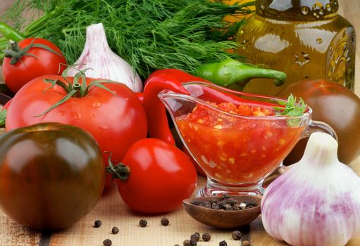 Arrangement of Bruschetta Sauce in Glass Gravy Boat with Black Tomatoes, Garlic, Chili Peppers and Olive Oil in Glass Bottle closeup on Wooden background. Horizontal View