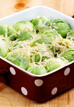 Delicious Homemade Brussels Sprouts Casserole in Brown Polka Dot Bowl with Grated Cheese and Spices closeup on Wooden background