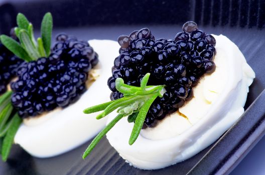 Snacks with Gourmet Black Caviar, Boiled Eggs and Rosemary closeup on Black Plate