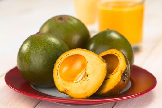 Peruvian fruit called Lucuma (lat. Pouteria lucuma), which has a dry, sweet flesh, and is mostly used to prepare juices, milkshakes, yogurts, ice cream and other desserts, served on a red plate with lucuma milkshake and jogurt in teh back (Selective Focus, Focus on the front of the first fruit) 