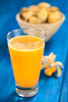 Freshly prepared juice made of physalis (lat. Physalis peruviana) served in glass with a basket full of physalis in the back (Selective Focus, Focus on the front of the glass rim)
