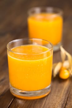 Freshly prepared juice made of physalis (lat. Physalis peruviana) served in glass with physalis fruits on the side (Selective Focus, Focus on the front of the glass rim)
