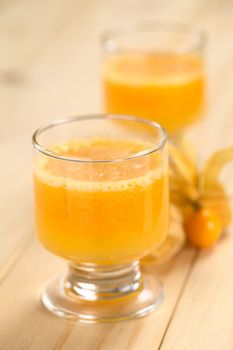 Freshly prepared juice made of physalis (lat. Physalis peruviana) served in glass with physalis fruits on the side (Selective Focus, Focus on  the front of the glass rim)
