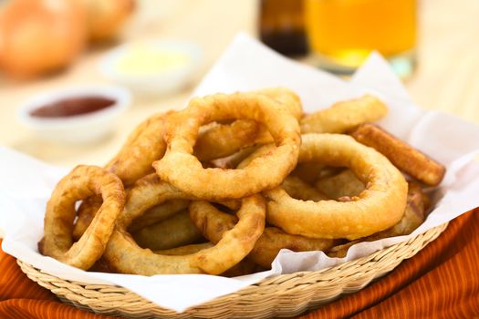 Freshly prepared homemade beer-battered onion rings in a basket with drinks and sauces in the back (Selective Focus, Focus on the front of the onion ring on the top)