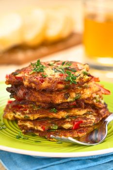 Vegetable and egg fritter made of zucchini, red bell pepper, eggs, green onions and thyme piled on a green plate with fork on the side (Selective Focus, Focus on the front of the thyme sprig on the top of the fritters and on the front of the top fritters) 