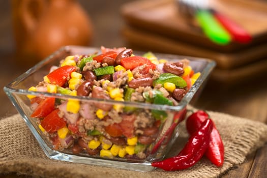 Chili con carne salad made of mincemeat, kidney beans, green bell pepper, tomato, sweet corn and red onions served in glass bowl (Selective Focus, Focus in the middle of the salad)