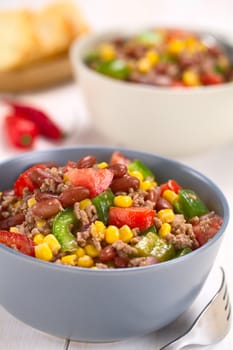 Chili con carne salad made of mincemeat, kidney beans, green bell pepper, tomato, sweet corn and red onions served in bowls with fork on the side (Selective Focus, Focus in the middle of the salad)