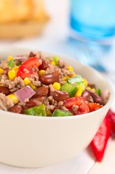 Chili con carne salad made of mincemeat, kidney beans, green bell pepper, tomato, sweet corn and red onions served in bowl with chili on the side (Selective Focus, Focus in the middle of the salad)