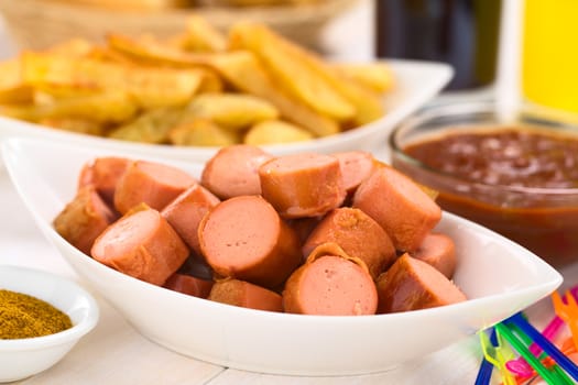 Fried sausage pieces with French fries and curry-ketchup-sauce in the back (Selective Focus, Focus one third into the sausages) 