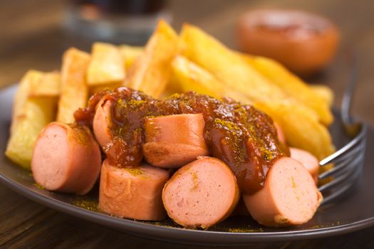 German fast food called Currywurst served with French fries on a plate with fork (Selective Focus, Focus on the front of the dish) 