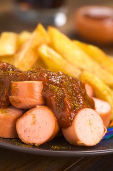 German fast food called Currywurst served with French fries on a plate (Selective Focus, Focus on the front of the sausage on top) 