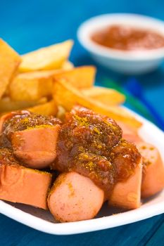 German fast food called Currywurst served with French fries on a disposable plate (Selective Focus, Focus on the front of the sausage on top) 